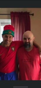 Two men smiling, one wearing a green elf hat.