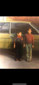 Two boys standing beside a vintage car, one holding a toy gun.