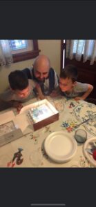 Two boys and a man leaning over a birthday cake with lit candles.