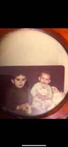 Two children sitting closely, one smiling and one serious.