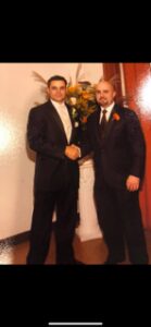 Two men in tuxedos shaking hands at a formal event.