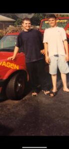 Two people holding hands beside a red vehicle with 'VAGEN' on it.