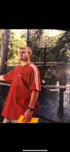 Man in red shirt standing near a fenced area with animals.