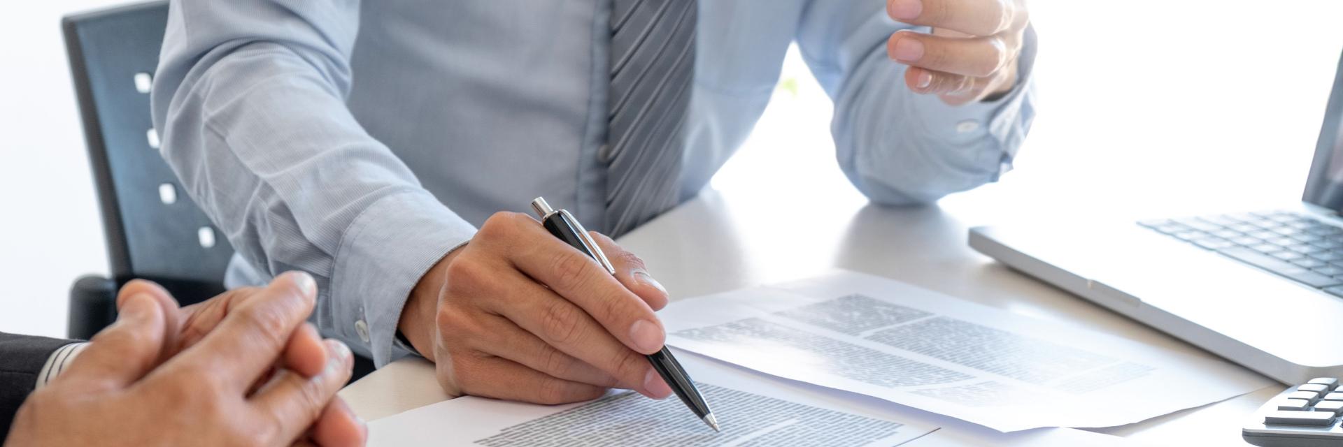 A person hovering a pen over a paper while talking to someone.