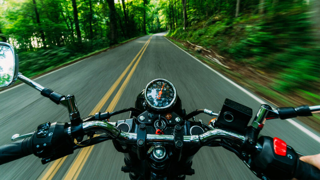 view from a motorcycle speeding down a forested road - https://brancoinsurancegroup.com/