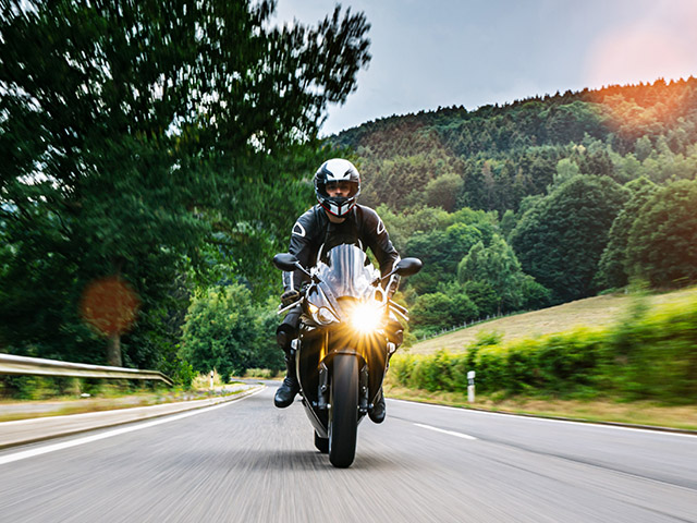 A motorcyclist dressed in black gear rides a bike down a winding road - https://brancoinsurancegroup.com/