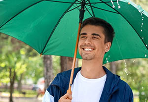 Smiling man under a green umbrella in a park - https://brancoinsurancegroup.com/