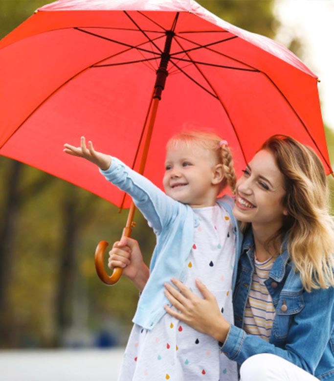 A smiling woman and child hold a red umbrella in a park