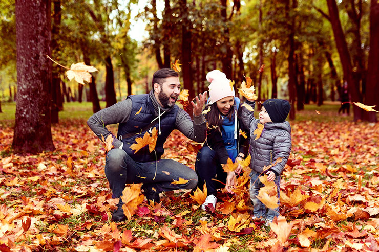A family of three joyfully playing with colorful autumn leaves in a park during the fall season