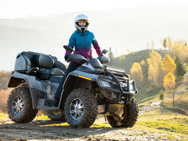 A woman confidently rides an ATV along a rugged dirt road surrounded by greenery