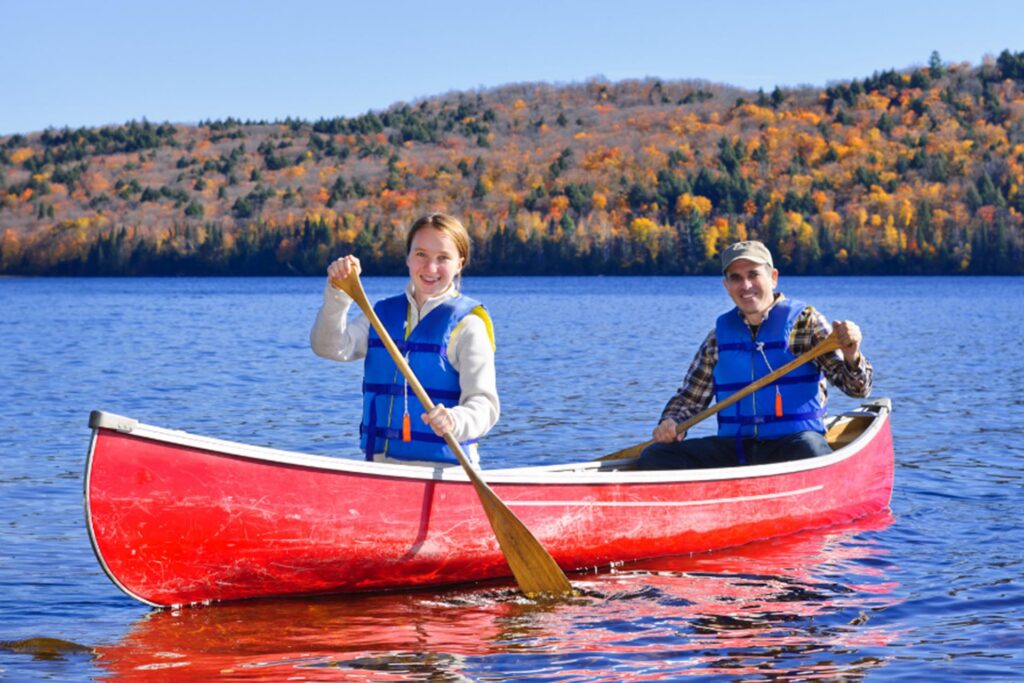 A man and a woman paddling together in a canoe on a calm lake surrounded by trees
