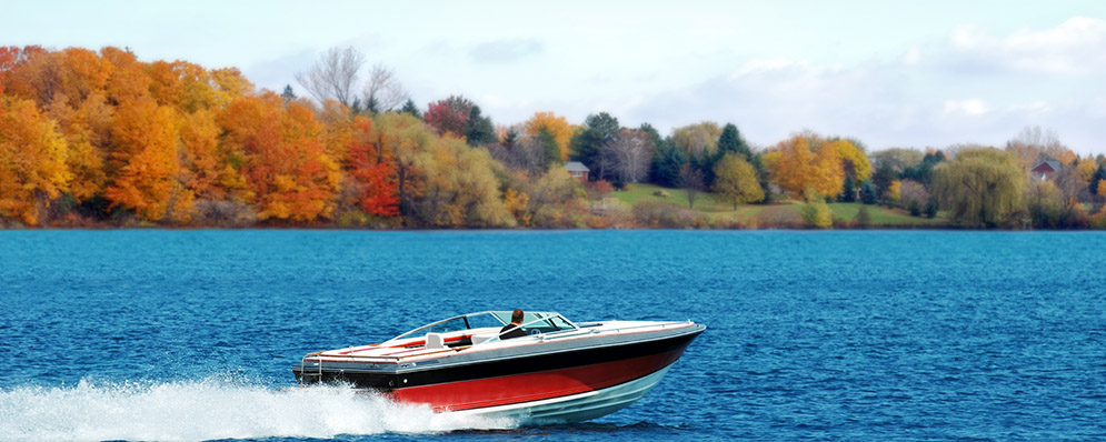 A speed boat glides across the water, framed by vibrant autumn trees in the background.