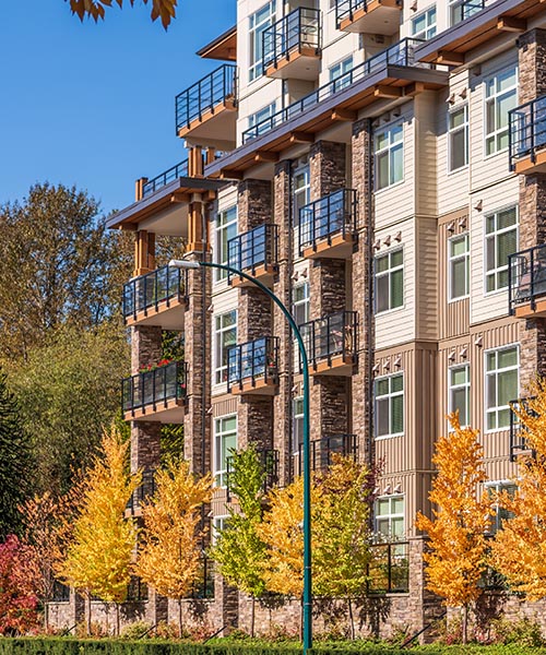 A large apartment building featuring multiple balconies surrounded by lush green trees