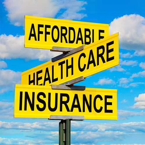 Yellow street signs with Affordable Health Care Insurance against a blue sky.