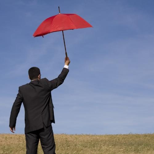 Man in suit holding a red umbrella against a clear blue sky.