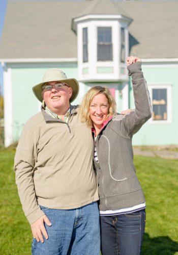 Insured man and woman posing happily with their house in the background.