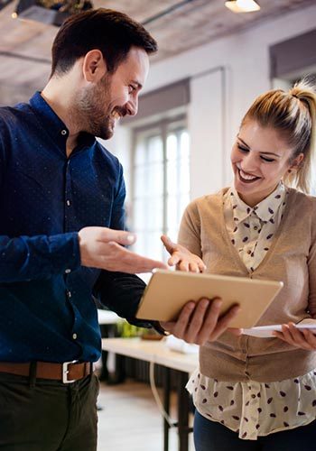 A man and woman stand in an office, examining a tablet together with focused expressions
